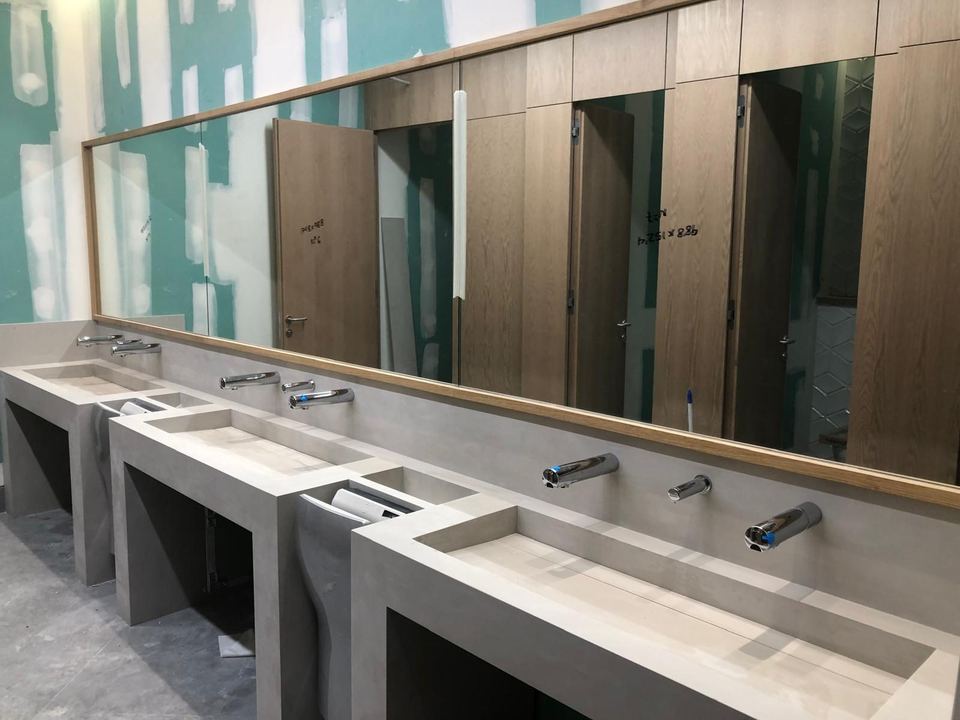 Baño público con grifería electrónica y espejo instalados