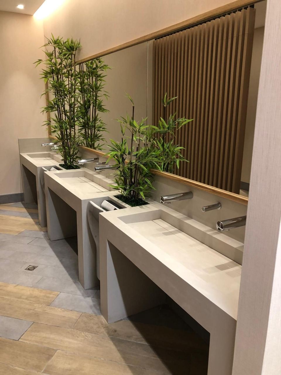 Baño público terminado con lavabos, plantas y revestimiento de madera